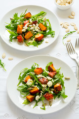 Fresh autumn salad with baked pumkin, arugula, cheese and seeds on white table cloth. Space for copy