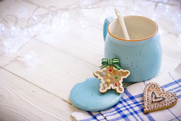 Christmas still life. On the table is a blue cup with cookies in the form of a star and a heart. In the background are beautiful white garlands.