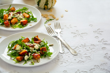 Fresh autumn salad with baked pumkin, arugula, cheese and seeds on white table cloth. Space for copy