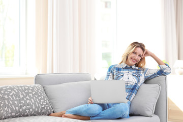 Beautiful young woman with modern laptop on sofa at home