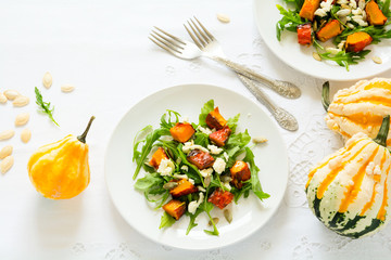 Fresh autumn salad with baked pumkin, arugula, cheese and seeds on white table cloth. Space for copy
