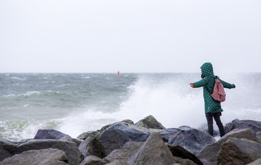 eine Frau steht bei starkem Sturm an der Küste eines Meeres