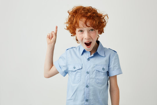 Close up of funny ginger boy with freckles pointing apside on white background with opened mouth and silly face expression. Copy space