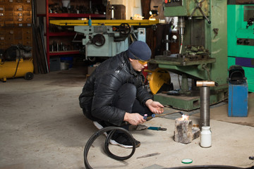 Work man is a welder in mask, metal product at home garage, with flame burning gas welding