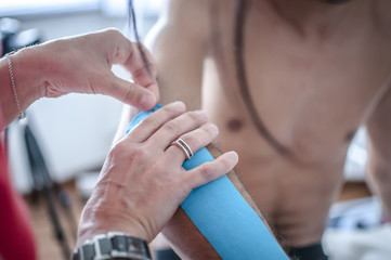 fisioterapista applica tape dopo massaggio per il dolore a un giovane sportivo
