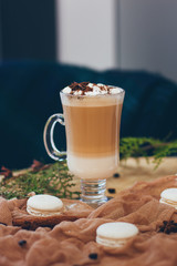 A glass of cappuccino with marshmallow on the brown cloth with macaroons, cinnamon sticks, anise in Christmas atmosphere
