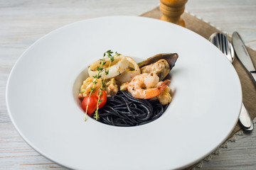Italian black spaghetti with cuttlefish ink, mussels, tomatoes and green basil on the table.
