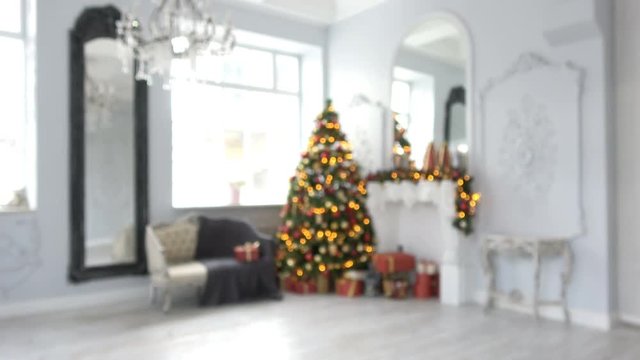 4K video footage of unfocused classic white room with Christmas and New Year interior decoration. Green tree decorated with toys and flashing garland.