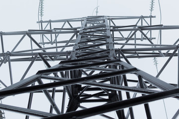 Closeup atmospheric photo of the high voltage transmission tower covered with hoarfrost standing on the gray sky background after blizzard