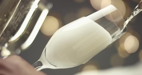 Close up video of pouring sparkling glass into a flute glass, foam overflowing on gray background with golden lights - Powered by Adobe