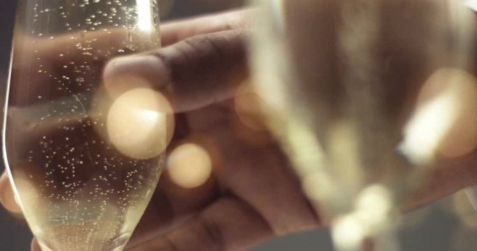 Close up of a man's hand picking up a flute glass with sparkling wine with bubbles in gray and gold tones