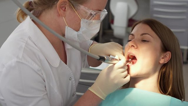 Dentist treating teeth to woman patient in clinic. Female professional doctor stomatologist at work. Dental equipment on background. Dental check up