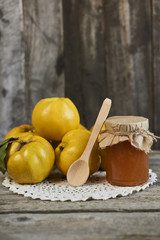 jar of jam with spoon and quinces with leaves on wooden rustic background