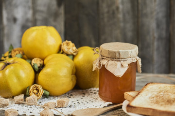 jar of jam with sandwich and quinces with leaves on wooden rustic background
