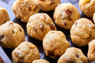 Traditional national Indian homemade sweets Rava ladoo. Oriental candies with own hands. Sweet delicious dessert with nuts and raisins. Dessert of milk powder on a baking sheet on a wooden table.
