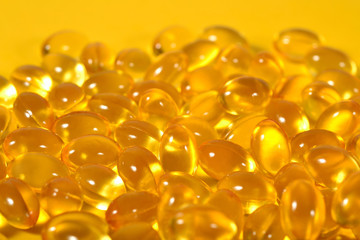 Omega-3 fish fat oil capsules close up on a yellow background.