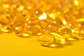 Omega-3 fish fat oil capsules close up on a yellow background.