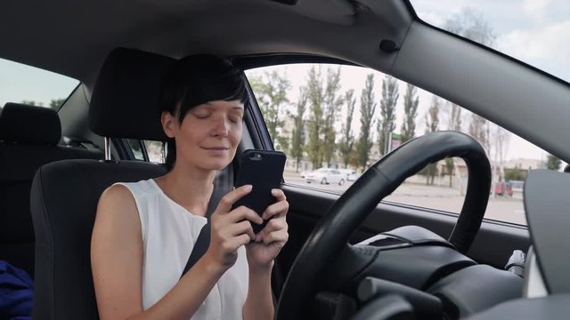 adult caucasian woman sitting in car on driver’s seat using smartphone. Attractive female messaging or surfing internet. Girl chatting with friend before driving