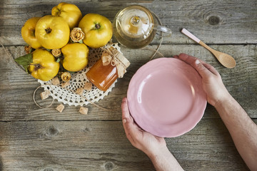 masculine hands holding empty plate with jar of jam and quinces on rustic wooden background