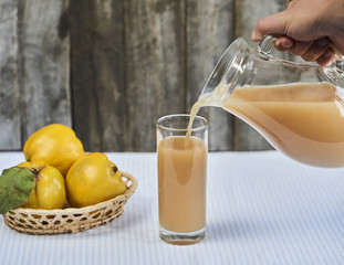 hands pours orange juice with quince on rustic wooden background