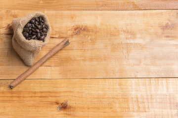 Coffee bean on small sack of brown and cinnamon over wooden table board, copy space, presentation product, top view