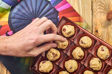 A man takes a homemade candy from a festive box. Bright rainbow background. Traditional national Indian homemade sweets Rava ladoo. Oriental candies.