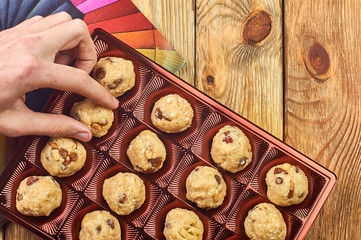 A man takes a homemade candy from a festive box. Bright rainbow background. Traditional national Indian homemade sweets Rava ladoo. Oriental candies.