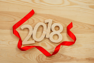 Wooden figures forming 2018, carved from light wood on the background of old wood. Tie the red ribbon. New Year Idea, postcard, poster, greetings.