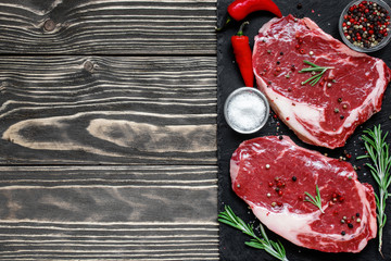 Raw meat, beef steak with spices and rosemary on black slate board