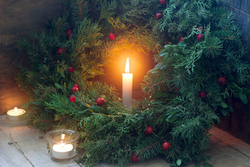 A Christmas wreath made of fir branches, juniper, tuja, boxwood and wild rose berries. Wreath with burning candles.