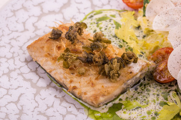 The sturgeon cooked on a grill with creamy sauce with tomatoes and cabbage