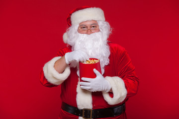 Fototapeta na wymiar Traditional Santa Claus watching TV, eating popcorn. Christmas. Red background. emotions fear surprise