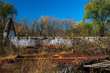A long wall of an old abandoned ruined brick house in thickets. The debris of an old building. A sunny day, autumn, Ukraine