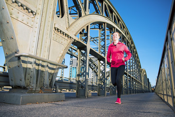 Young, sexy woman is running along a Bridge and doing her Sport exercise