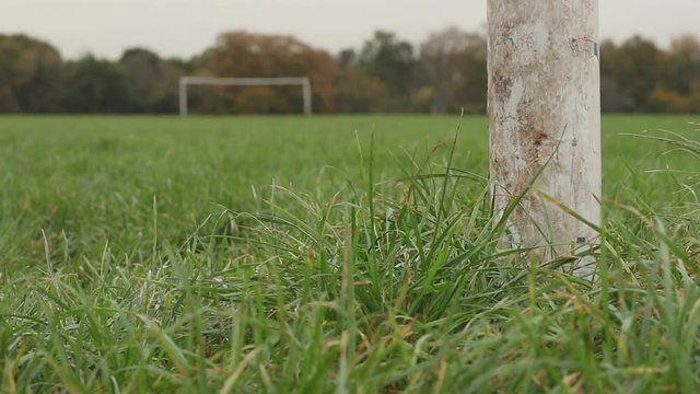 Grassy playing field, close-up on goalpost. Opposite goalpost visible in distance, out-of-focus. 1080p video at 25fps