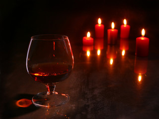 christmas decoration. glass of cognac or whiskey and red candle on a wooden background.