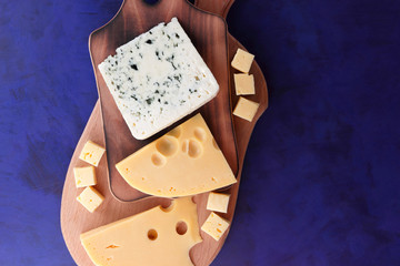 Yellow cheese, hard cheese with holes, Polish cheese, cheese with a mold on a wooden board, different cheeses on a dark blue background in a minimalist style, retro style