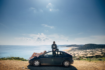 Fototapeta na wymiar Couple sitting on a car, sea and mountain on background