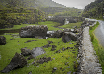 Fototapeta na wymiar Vue de la Black Valley dans le parc de Killarney. Une route enjambe un pont, le long de la Black river qui serpente dans des gorges sur fond de verdure et de nuages. 