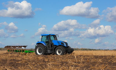 Obraz premium a large blue tractor, plowing field against the beautiful sky. Work of agricultural machinery. Harvest