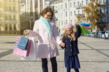 Mom and children are happy shopping. Pose background is square European city, holding shopping bags.