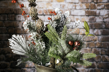 winter bouquet of plants and berries with red and gold bells covered in frost in metal pitcher with brick wall background
