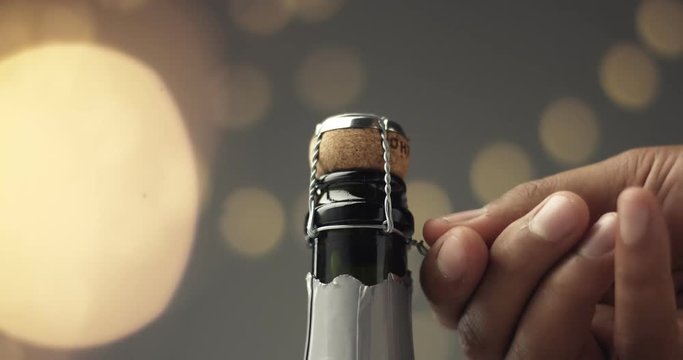Close up video of man's hands opening a bottle of champagne on gray background with lights and flares