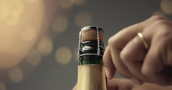 Close up video of man's hands opening a bottle of champagne on gray background with lights and flares