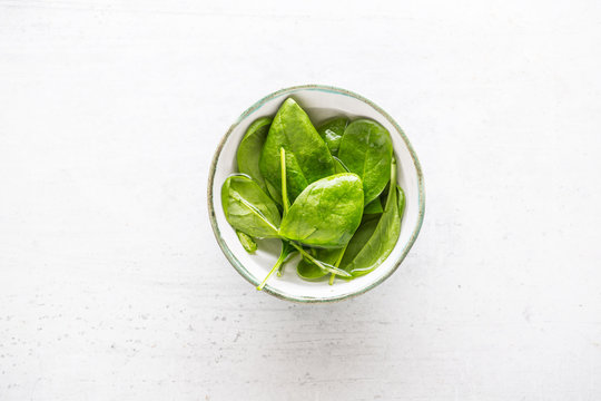 Top of view fresh spinach leaves in bowl on white concrete board