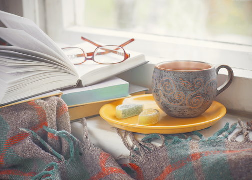 Cozy morning at home. A cup of tea, a blanket, old books and glasses on the windowsill, selective focus.