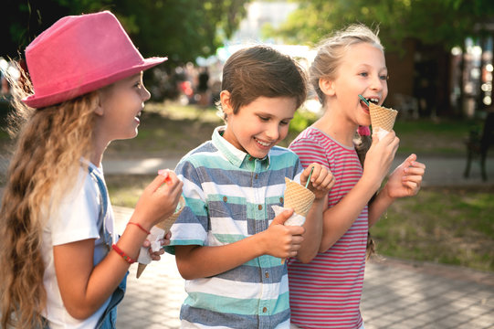 Close-up portrait of three happy preteen children walking on the street, having fun and eating ice-cream
