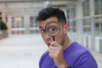 Shocked curious young male looking through a loupe