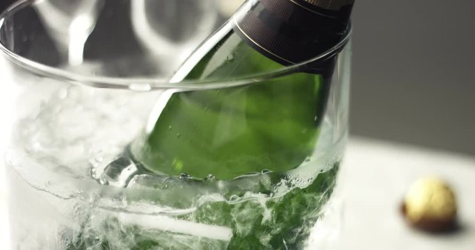 Green glass bottle of sparkling wine in a clear glass ice bucket on a table with white tablecloth
