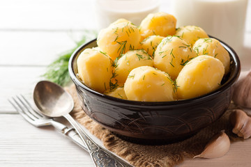 Boiled potatoes with dill in bowl on white wooden background.